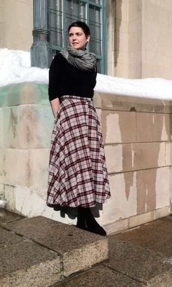 a woman standing on steps in front of a building wearing a black sweater and plaid skirt