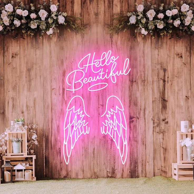 a pink neon sign that says hello beautiful with angel wings in front of a wooden wall