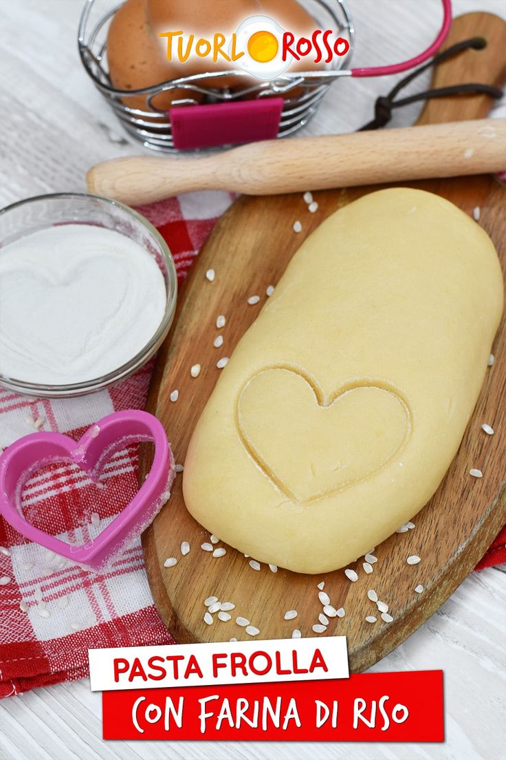 a heart shaped cookie sitting on top of a wooden cutting board next to baking utensils