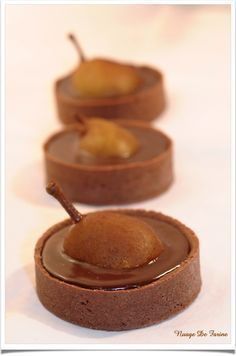 three chocolate desserts with two pears on top and one in the middle, sitting next to each other