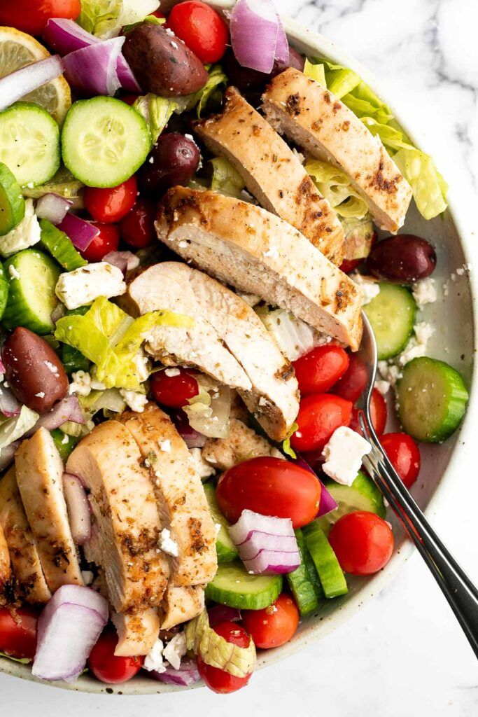 a salad with chicken, cucumbers, tomatoes, onions and olives