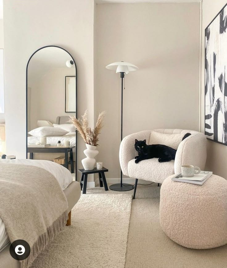 a black cat laying on top of a white chair in a bedroom next to a bed