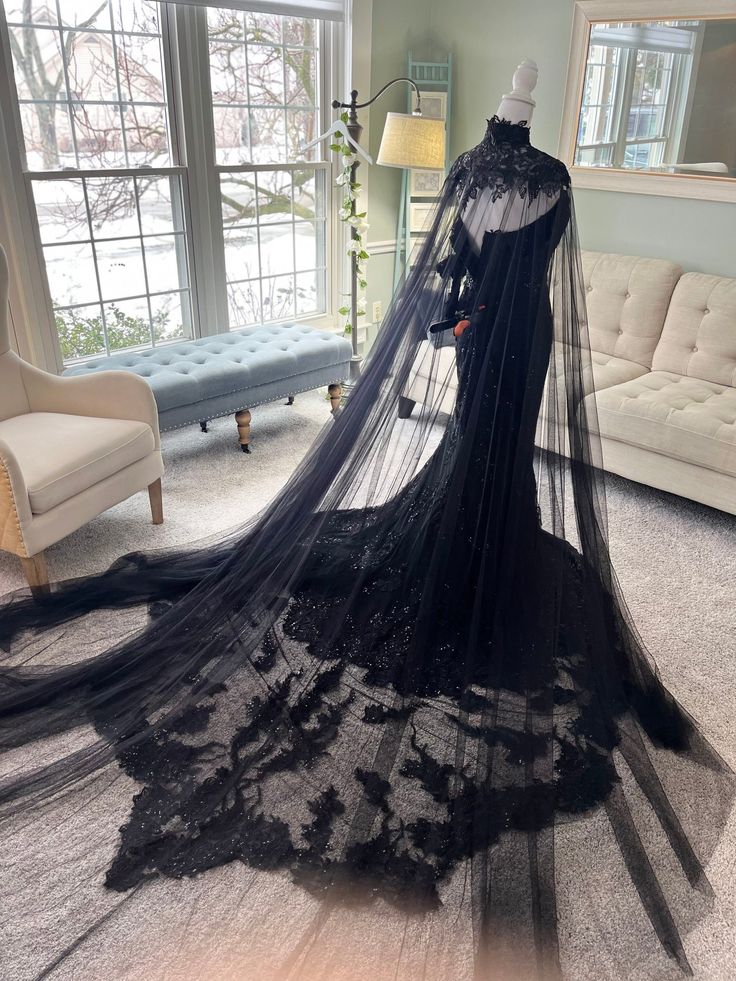 a black wedding gown with long veil on display in front of a couch and window