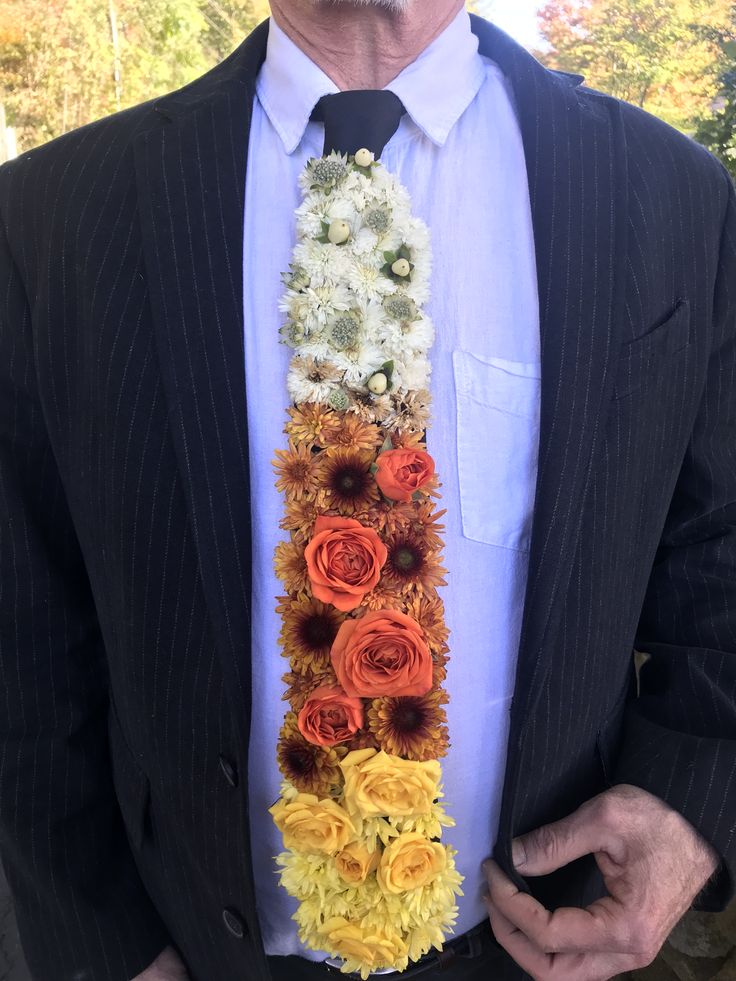 an older man wearing a suit and tie with flowers on the front, while holding his hands in his pockets