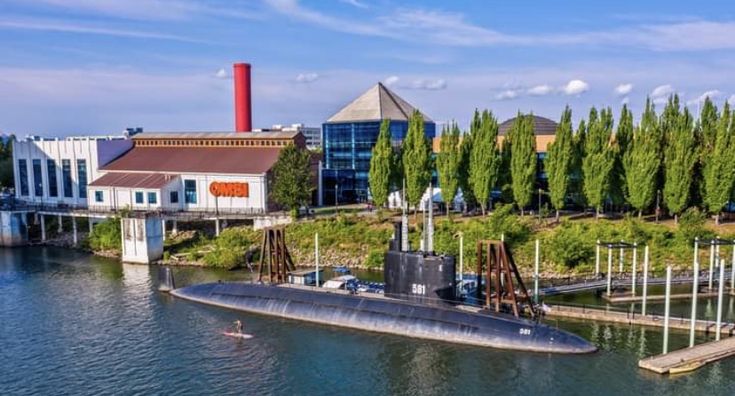 a large submarine floating on top of a river next to a bridge and buildings in the background