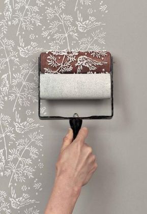 a person using a paint roller to paint a wall with white flowers on the background