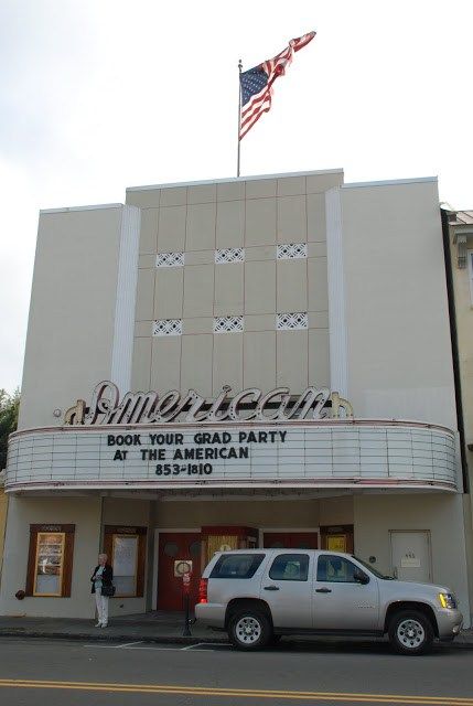 a white truck parked in front of a movie theater with an american flag on top