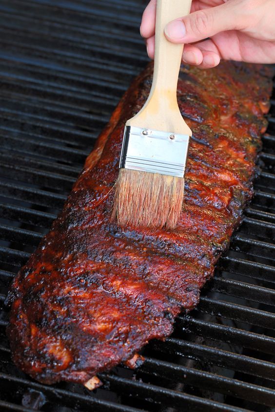 a person using a brush to clean the ribs on a bbq grill with charcoal