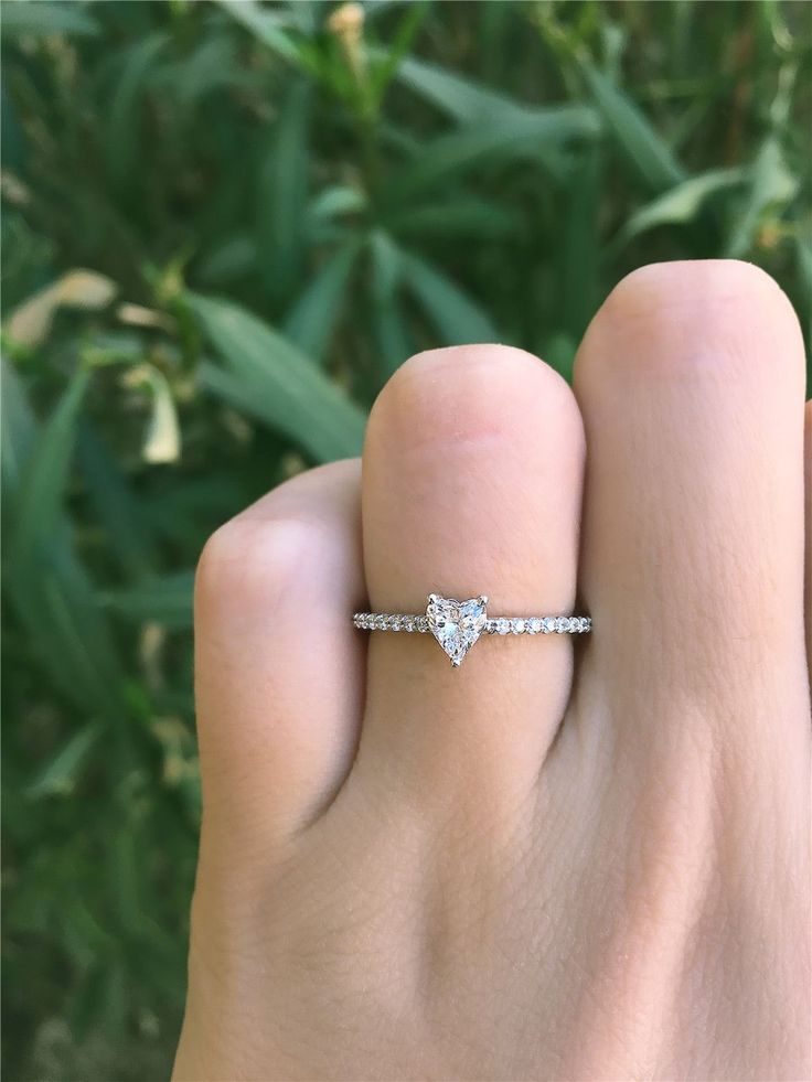 a woman's hand with a diamond ring on her finger and green plants in the background