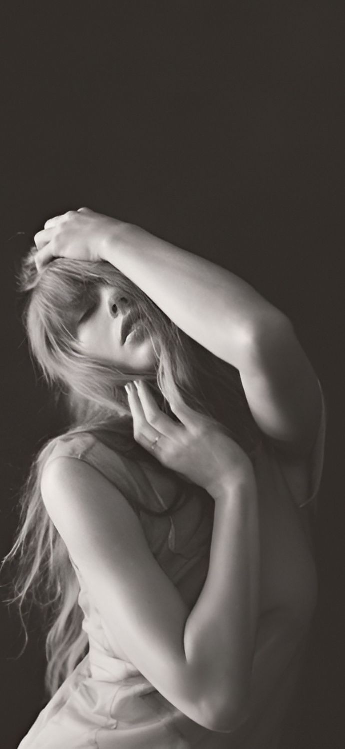 black and white photograph of a woman with her hands on her head, posing in front of a dark background