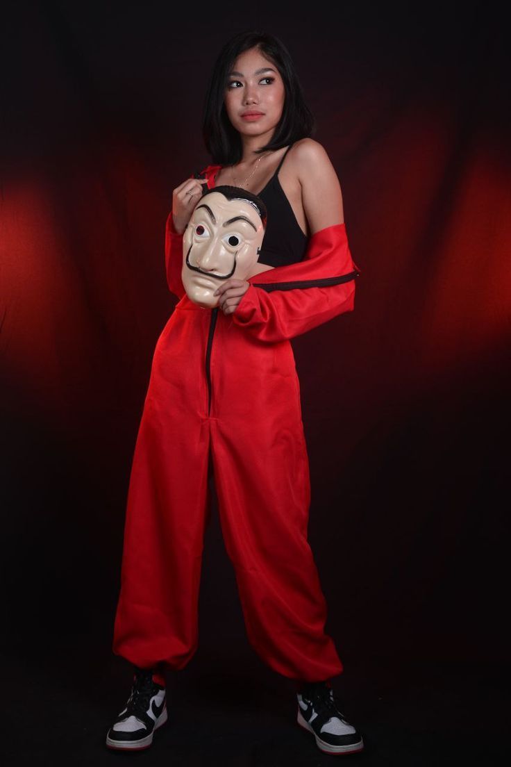 a woman in red pants holding a monkey mask