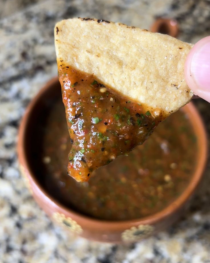 a hand holding a tortilla chip over a bowl of salsa