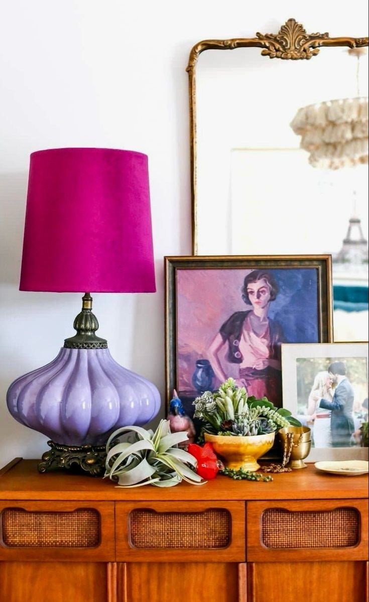 a purple lamp sitting on top of a wooden dresser next to a mirror and framed photograph