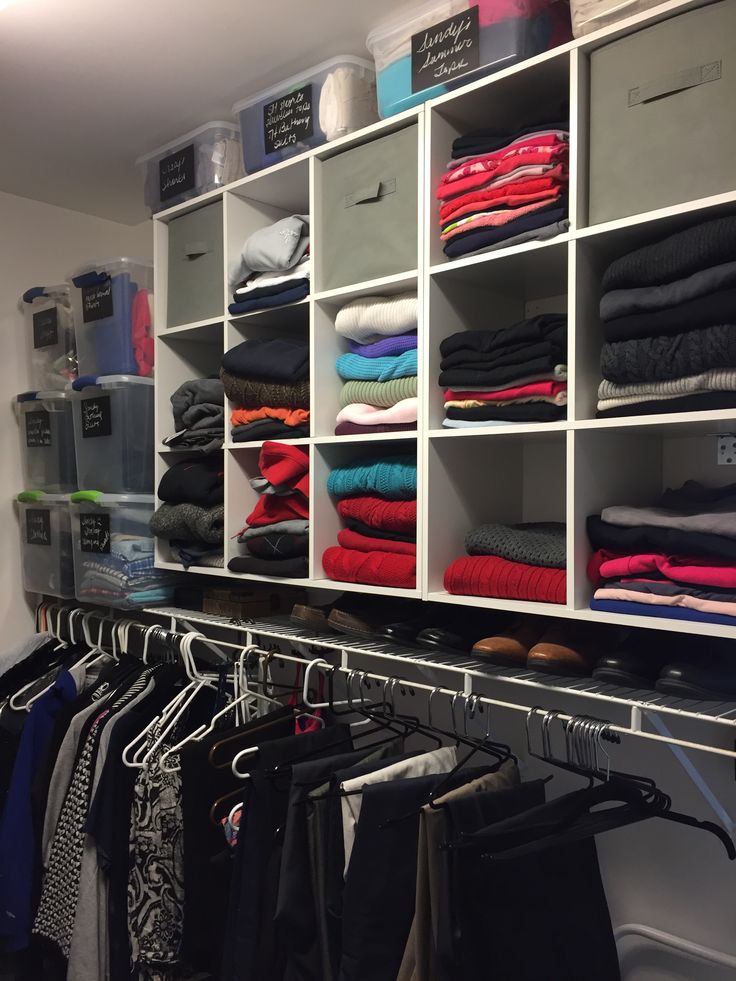 an organized closet with clothes hanging on shelves and bins full of folded shirts, pants and sweaters