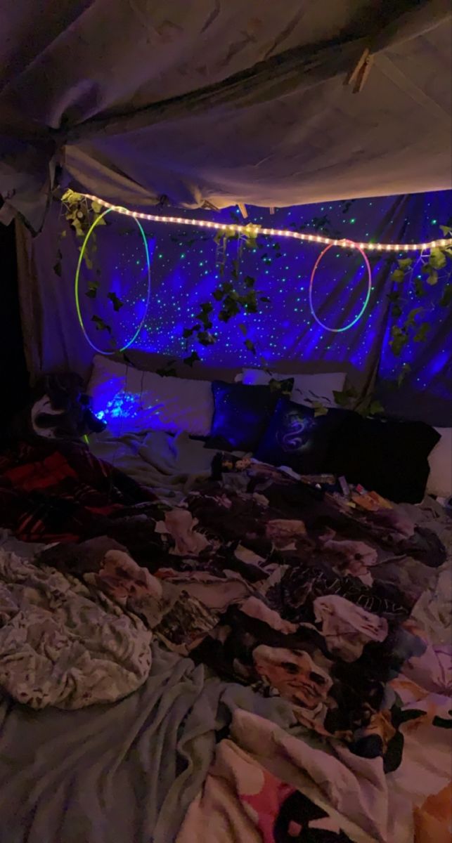 an unmade bed in a room with blue lights on the ceiling and clothes strewn about