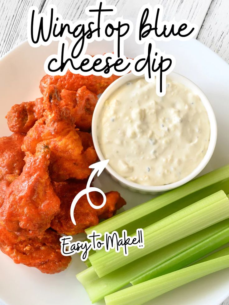 a white plate topped with wings and celery next to a bowl of dip