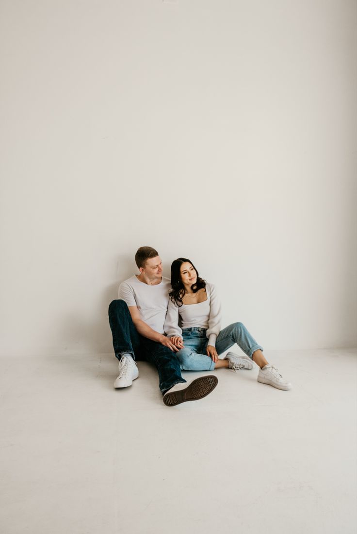 a man and woman are sitting on the floor in front of a white wall together