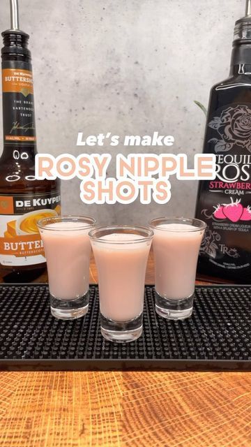 three shot glasses filled with liquid sitting on top of a wooden table next to bottles