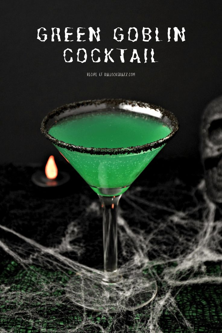 a green cocktail sitting on top of a table next to a candle and spooky spider web