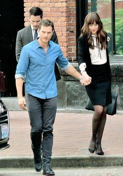 a man and woman holding hands walking down the street in front of a black car