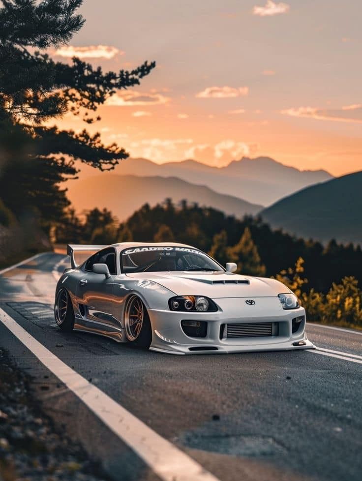 a white sports car parked on the side of a mountain road at sunset with mountains in the background