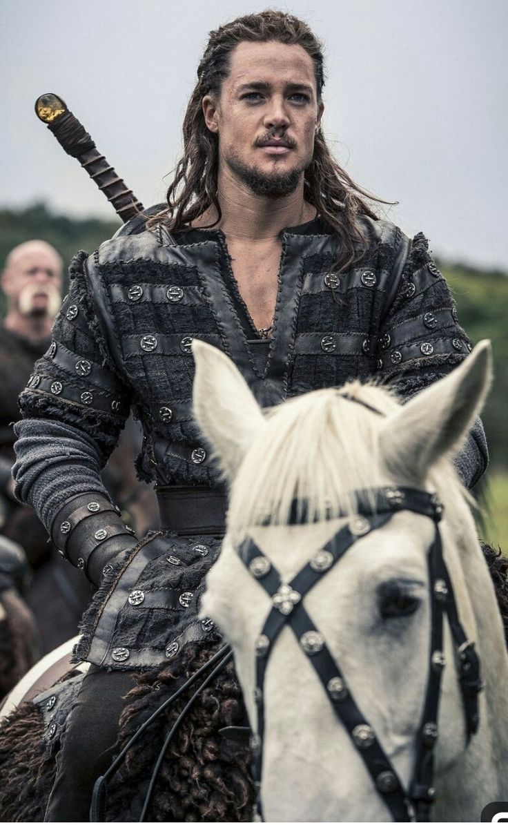 a man riding on the back of a white horse next to another man wearing armor