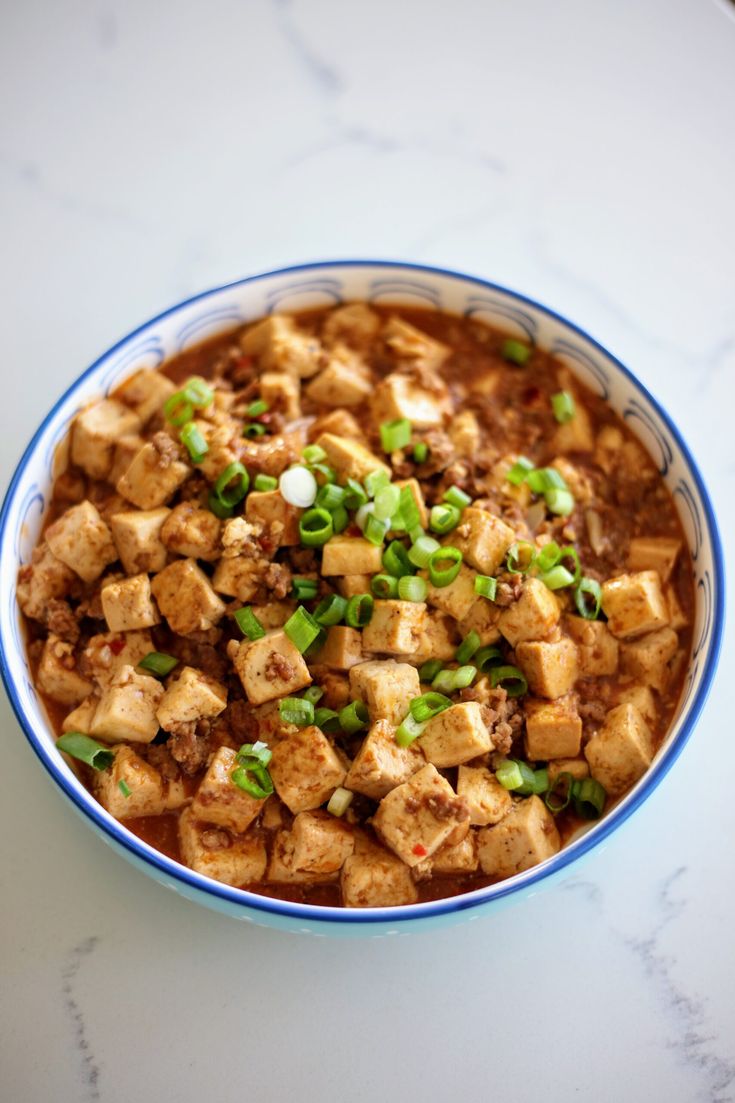 a bowl filled with tofu and green onions on top of a white countertop