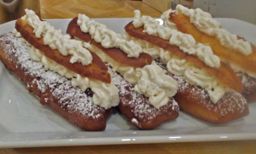 three pastries on a white plate with powdered sugar and whipped cream toppings