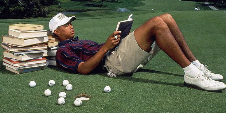 a man laying on the ground reading a book next to piles of books and golf balls