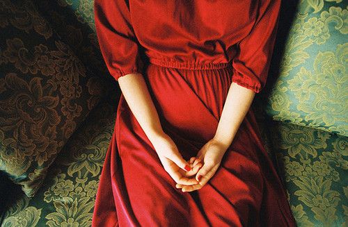 a woman in a red dress is sitting on a green couch with her hands together