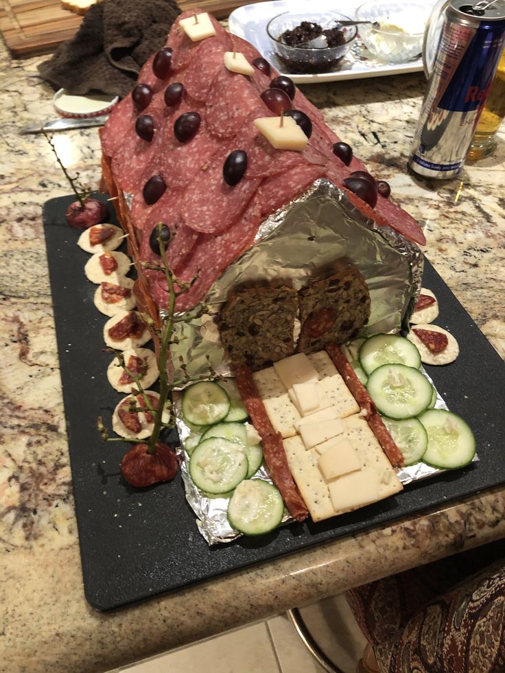 a table topped with a cake covered in meat and cheese next to cucumbers