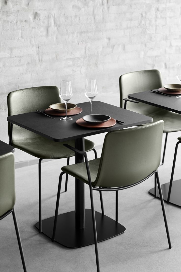 a dining table with four chairs and two wine glasses on top of it, in front of a white brick wall