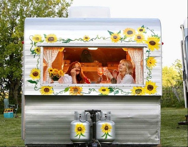 two women sitting in the window of a trailer with sunflowers painted on it