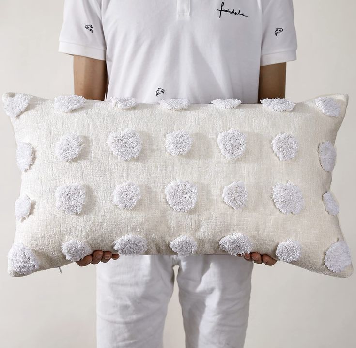 a man holding a pillow with white pom - poms on it