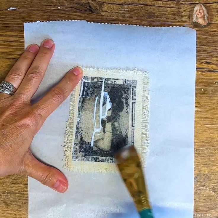 a person's hand holding a brush over a piece of paper with an image on it