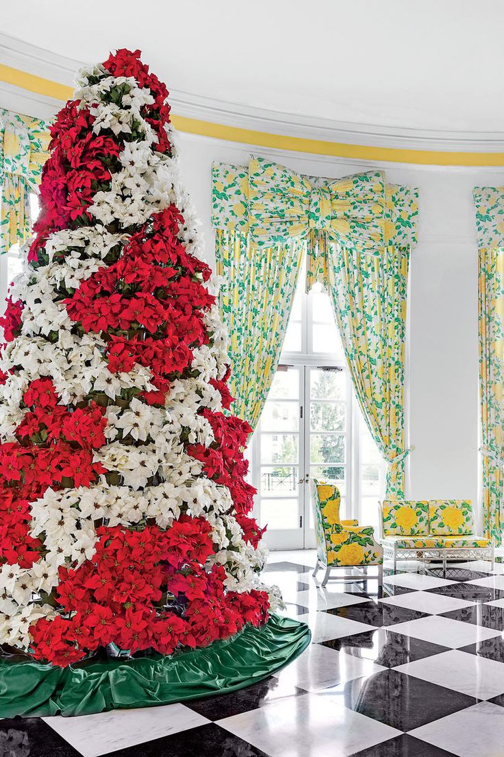 a large christmas tree with red and white flowers on it's base in the middle of a black and white checkered floor