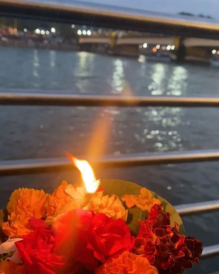 a close up of a lit candle with flowers in front of the water and bridge