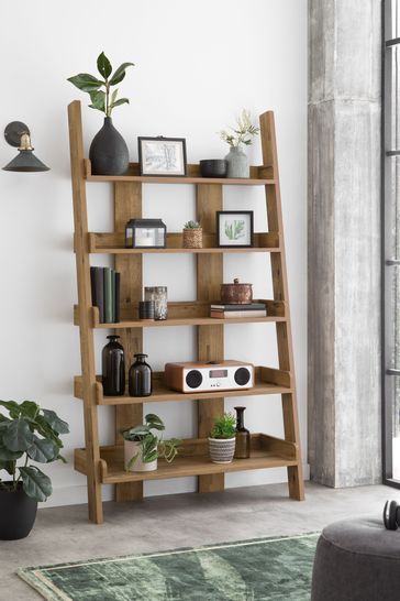 a wooden shelf with plants and pictures on it in front of a window, next to a couch