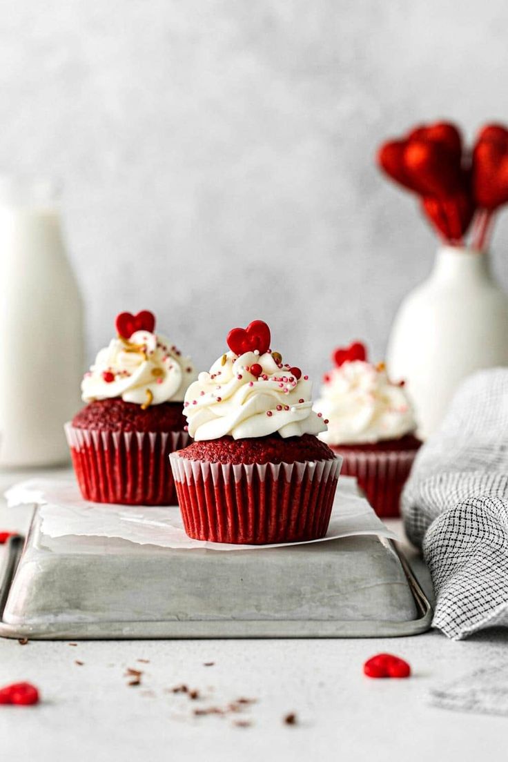 three red velvet cupcakes with white frosting and sprinkles on a tray