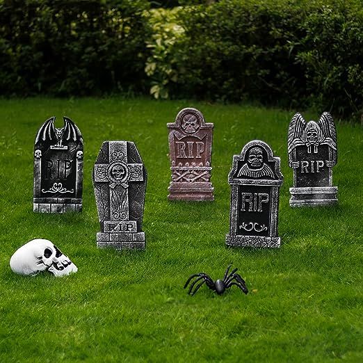 halloween tombstones in the grass with a fake skull and spider on the ground next to them