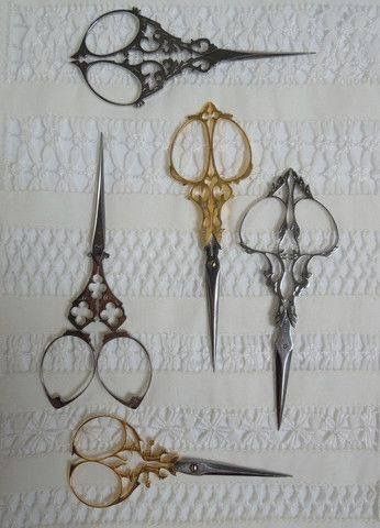 five pairs of scissors are sitting on a white lace tablecloth, each with different shapes and sizes