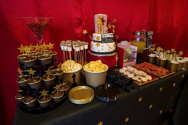 a table topped with lots of food and desserts next to a red curtained wall