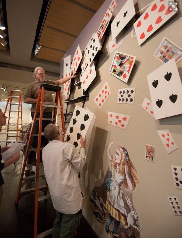 two men are working on playing cards on the wall while another man is standing up