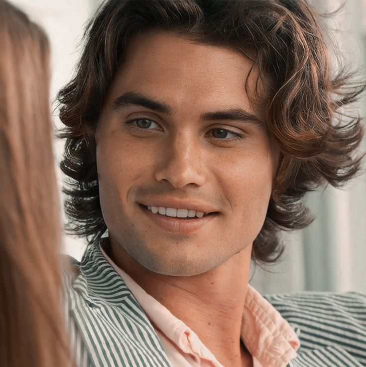 a close up of a person wearing a suit and smiling at another person with long hair