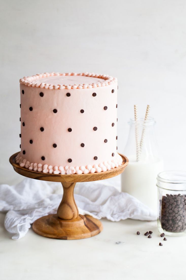 a pink cake sitting on top of a wooden stand next to a bottle of milk