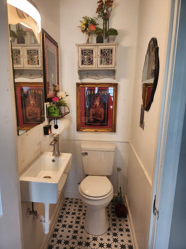 a white toilet sitting next to a sink in a bathroom under pictures on the wall