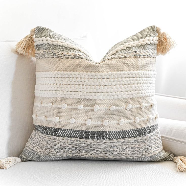 a pillow with tassels on it sitting on a white couch next to a window