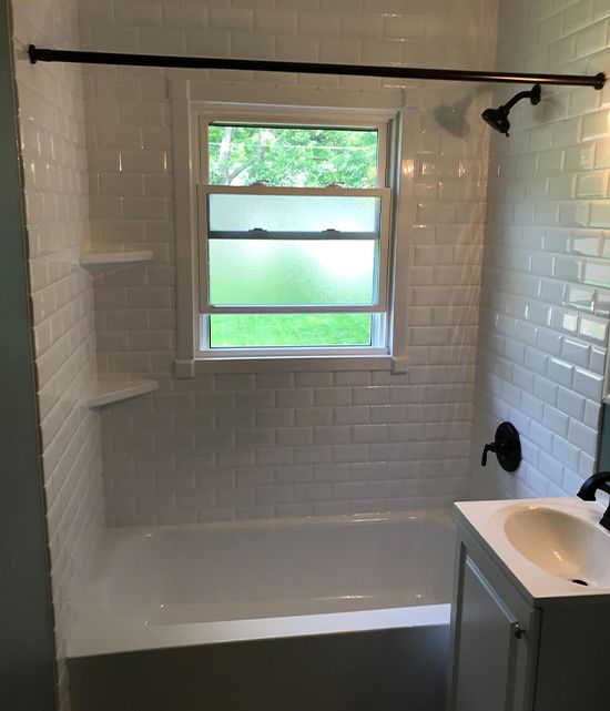 an empty bathroom with white tile walls and flooring, along with a window above the bathtub