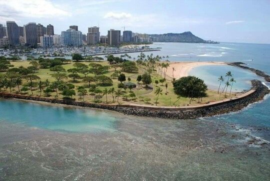 an island in the middle of some water with buildings and trees around it on one side