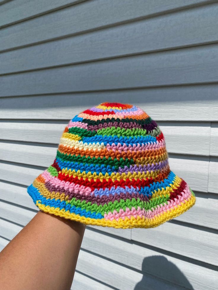 a multicolored crocheted hat is being held up by someone's hand